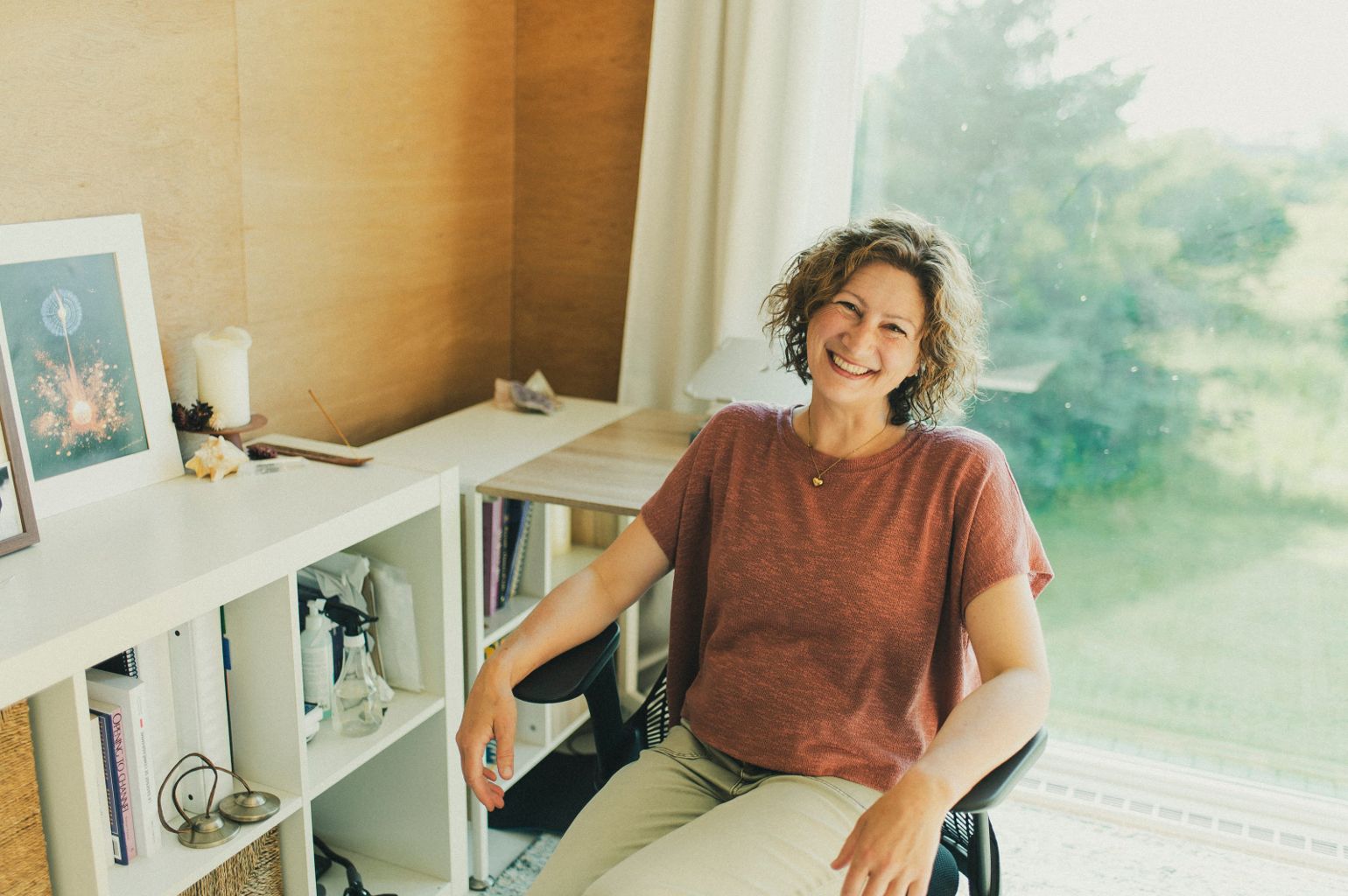 Christine Dion souriante dans son bureau baigné de lumière naturelle, mur de bois clair et verdure à la fenêtre.